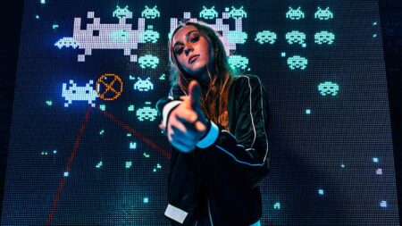 Gamer girl doing finger gun pose in front of Space Invaders backdrop in an arcade