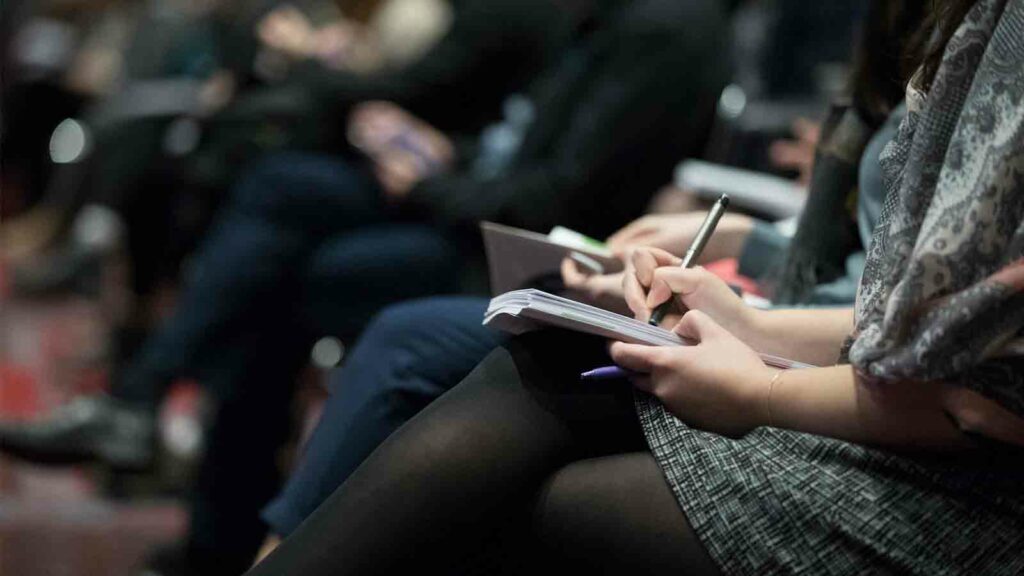 Woman holding a pen writing in her notebook at a business conference